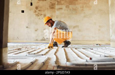 Arbeiter in gelber Uniform, der Fußbodenheizungen installiert Stockfoto