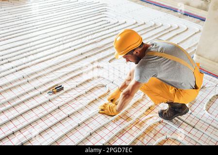 Arbeiter in gelber Uniform, der Fußbodenheizungen installiert Stockfoto