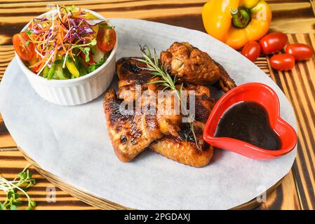 Gebratene Hähnchenflügel serviert Gemüsesauce und Sauce auf weißem Teller, Nahaufnahme von der Seite Stockfoto