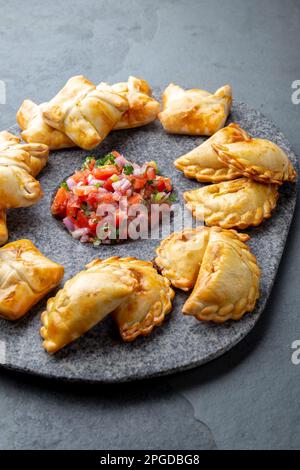 Verschiedene kleine Cocktail EMPANADAS auf der Steinplatte mit Tomatensauce und Guacamole. Grauer Hintergrund. Lateinamerikanische und Spanische typische Lebensmittel Stockfoto