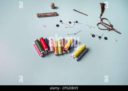 Neue Rollen aus mehrfarbigem Faden auf einer glatten blauen Oberfläche mit Nadeln, Nadeln, schwarzen und weißen Knöpfen und einer alten Schere Stockfoto