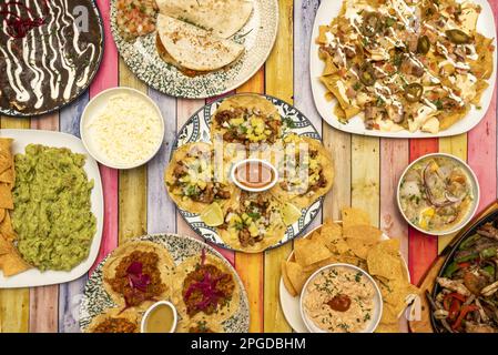 Teller mit mexikanischen Rezepten mit Tacos aller Art auf Weizen- und Maistortillas, Quesadillas, Drahteintopf, Ceviche, geriebenem Käse und farbigem Ta Stockfoto