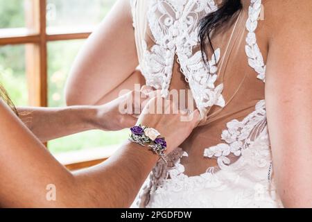Die Hände der Brautmutter knöpfen das Kleid Stockfoto