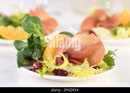 Portionierte Vorspeise mit Prosciutto-Schinken, serviert auf einer Mischung aus Orangen und Granatapfel. Stockfoto