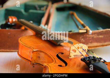 Alte Geige und Bogen liegen über dem offenen, abgenutzten Etui. Selektiver Fokus. Stockfoto