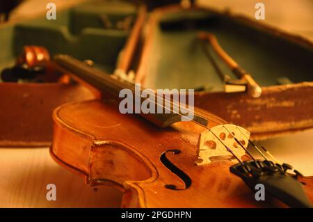 Alte Geige und Bogen liegen über dem offenen, abgenutzten Etui. Selektiver Fokus. Stockfoto