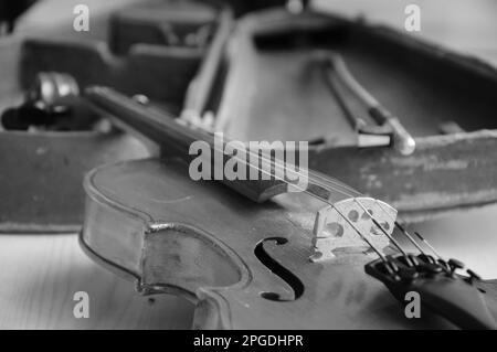 Alte Geige und Schleife, die über einem offenen, verschlissenen Koffer lagen. Selektiver Fokus auf F-Löcher und Brücke. Veraltetes Foto. Schwarz auf Weiß. Stockfoto