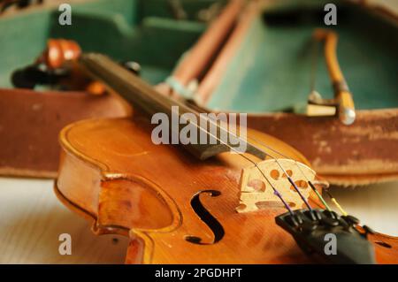 Alte Geige und Bogen liegen über dem offenen, abgenutzten Etui. Selektiver Fokus. Stockfoto