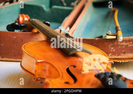 Alte Geige und Bogen liegen über dem offenen, abgenutzten Etui. Selektiver Fokus. Stockfoto