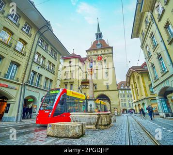 BERN, SCHWEIZ - 31. MÄRZ 2022: Rote Straßenbahn auf der Marktgasse, vorbei am mittelalterlichen Anna-Seiler-Brunnen, am 31. März in Bern, Schweiz Stockfoto