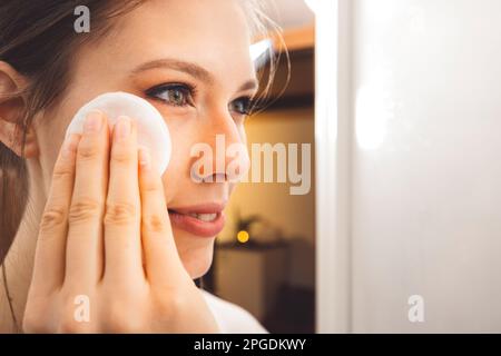 Nahaufnahme der Seite einer jungen Frau, die mit einem Wattepad und Mikellarwasser Make-up aus ihrem Gesicht entfernt Stockfoto