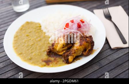 Hähnchenflügel mit pürierten Erbsen, Reis und eingelegten Zwiebeln auf weißem Teller Stockfoto