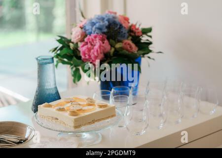 Käsekuchen mit blauen und rosa Blumen auf dem Hintergrund. Blumenstrauß in Vase. Stockfoto
