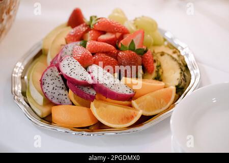 Obstsalat mit Erdbeeren, Orangen und Pitaya auf einem Teller auf einer weißen Tischdecke, Nahaufnahme Stockfoto