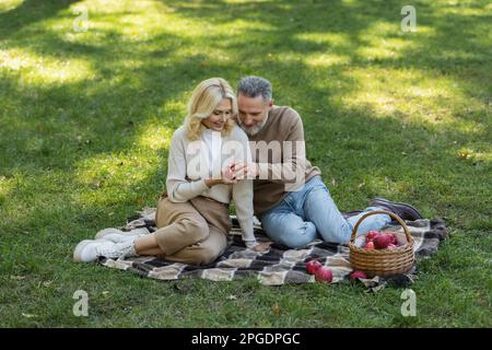 Glücklicher Mann und Frau mit rotem Apfel und sitzen auf einer Decke während des Picknickens im Park, Stockbild Stockfoto