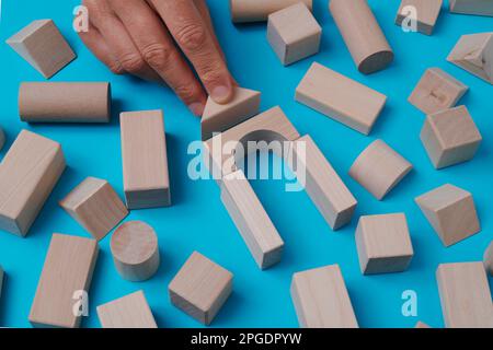 Ein Mann, der ein Haus mit ein paar Holzbausteinen auf blauem Hintergrund bildet, umgeben von ein paar weiteren Bausteinen Stockfoto