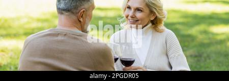 Ein nettes Paar mittleren Alters, das Gläser mit Rotwein im grünen Park, Banner, Stock Image Stockfoto