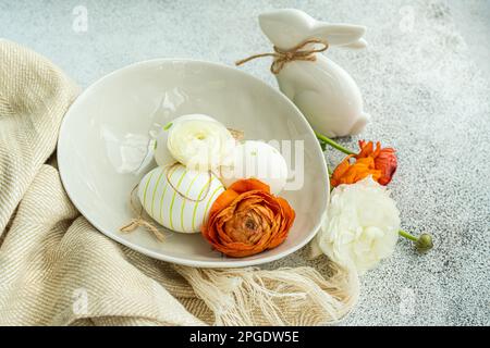 Nahaufnahme von bemalten Ostereiern, einem Osterhasen und orangefarbenen Ranunculus-Blumen Stockfoto