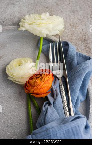 Nahaufnahme der orangefarbenen und weißen Ranunculus-Blüten auf einem Teller mit Besteck Stockfoto