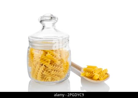 Rohes Fusilli in Glasgefäß und Holzlöffel mit Nudeln auf weißem Hintergrund, Zutaten für die Zubereitung, traditionelle italienische Küche. Stockfoto