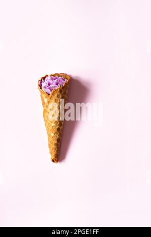 Waferkonus mit Tulpen auf pinkfarbenem Hintergrund. Blumeneis, Frühlingskonzept mit ersten Blumen. Stockfoto