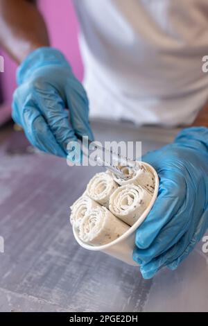 Ein Arbeiter legt Schokoladeneisbrötchen mit Zange und Latexhandschuhen in eine Wanne Stockfoto