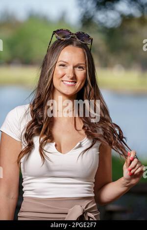 Foto einer attraktiven jungen Frau, die in die Kamera lächelt und mit ihrem Haar spielt Stockfoto