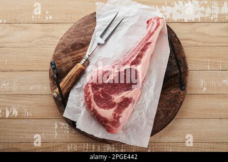 Frisches rohes Tomahawk-Steak. Trocken gereiftes rohes Tomahawk-Rindersteak mit Kräutern und Salz auf altem Holzhintergrund. Grillvorgang wird vorbereitet. Draufsicht und Kopierbereich. Stockfoto