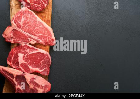 Rohe Prime Steaks. Auswahl an frischen schwarzen angus Prime Steaks T-Bone, New York, Ribeye, Striploin, Tomahawk Schneidebrett auf schwarzem oder dunklem Hintergrund Stockfoto