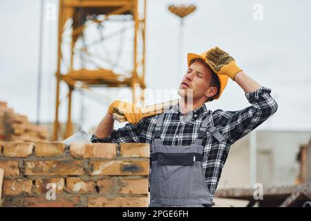 Hält das Messwerkzeug und legt eine Pause ein. Bauarbeiter in Uniform und Sicherheitsausrüstung arbeiten am Gebäude Stockfoto