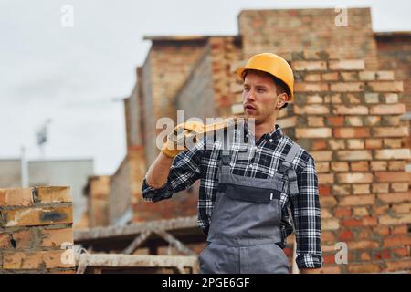 Hält das Messwerkzeug und legt eine Pause ein. Bauarbeiter in Uniform und Sicherheitsausrüstung arbeiten am Gebäude Stockfoto