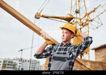 Transport von Holzbrettern. Bauarbeiter in Uniform und Sicherheitsausrüstung arbeiten am Gebäude Stockfoto