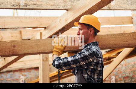 Transport von Holzbrettern. Bauarbeiter in Uniform und Sicherheitsausrüstung arbeiten am Gebäude Stockfoto