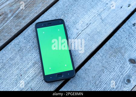 Ein Smartphone mit grünem Bildschirm liegt auf einem verblassten Holzhintergrund Stockfoto