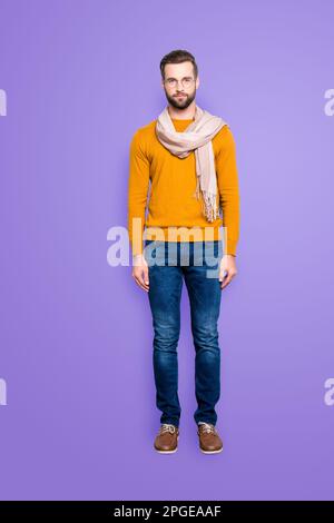 Ganzkörper-Porträt-Schnappschuss eines Strict Dreamy Stylist in Pullover-Jeans mit Schal um den Hals, der auf die Kamera blickt, isoliert auf grauem Hintergrund Stockfoto