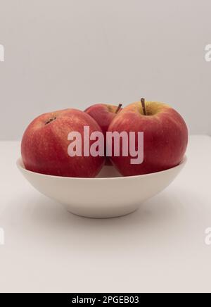 Drei kleine rote Äpfel in einem weißen Becher. Vertikal und Nahaufnahme. Stockfoto