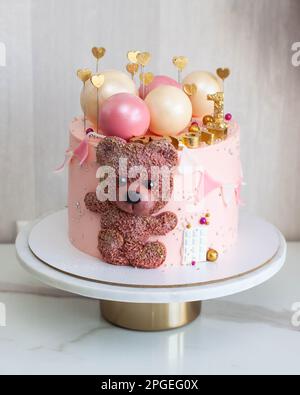 Zarter rosafarbener Kuchen zum Geburtstag des kleinen Mädchens mit Schokoladenkugeln, niedlichem Teddybär, goldenen Herzen und Nummer eins Stockfoto