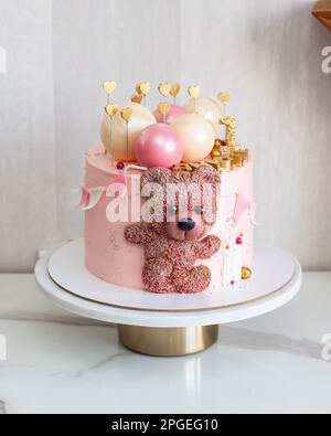 Zarter rosafarbener Kuchen zum Geburtstag des kleinen Mädchens mit Schokoladenkugeln, niedlichem Teddybär, goldenen Herzen und Nummer eins Stockfoto