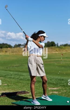 Vertikales, durchgehendes Porträt einer sportlichen Frau, die im Freien Golf auf grünem Gras spielt und einen schwingenden Golfschläger spielt Stockfoto