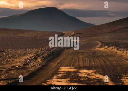 Leerer Feldweg und vulkanischer Berg nach Landmannalaugar inmitten abgelegener Wildnis am Abend im isländischen Hochland Stockfoto
