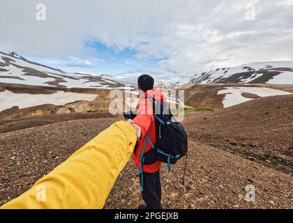 Ein Reisender mit Rucksack, der Hände hält, führt mit seiner Freundin in den Vulkanberg Kerlingarfjoll auf der geothermischen Gegend im Sommer in Island Stockfoto