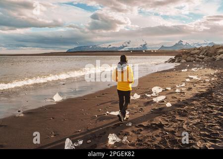 Junge asiatische Frau in gelber Jacke, die am Diamond Beach spaziert und im Sommer in Island Eisberg schmilzt Stockfoto