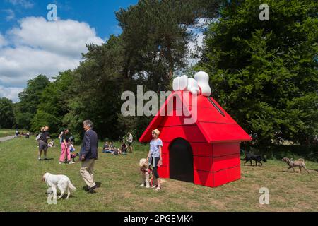 Leute machen Selfies mit ihren Hunden, die vor einer riesigen roten Hundehütte stehen, mit Snoopy auf dem Dach von Goodwoof, The Kennels, Goodwood, Sussex, Großbritannien Stockfoto