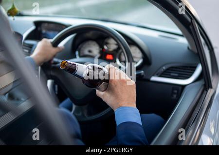 Ein Mann in einem teuren Anzug trinkt am Steuer eines Autos Bier, was die Gefahr eines Notfalls verursacht. Ein Geschäftsmann trinkt während der Fahrt. Betrunkener Fahrer Konz Stockfoto