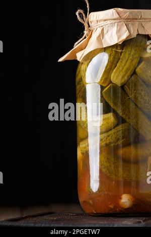 Eingelegte Gurken in einem geschlossenen Glasgefäß auf einer Holzfläche. Eingelegte Gurken mit Gewürzen aus der Nähe. Hausgemachte Gurkenkonserven Stockfoto