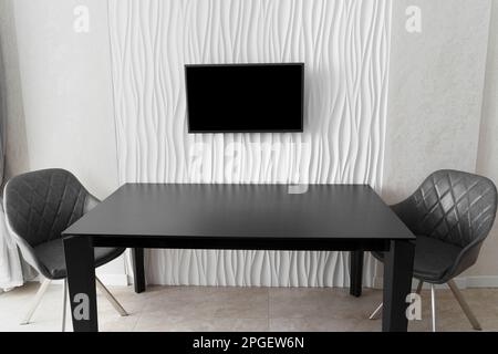 Minimalistisches Interieur. Ein großer Glastisch mit Stühlen an einer weißen Wand mit einem Fernseher in der Mitte. Küchendesign. Dinner-Zone Stockfoto