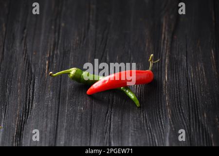 Rote und grüne Chili-Paprika auf dunklem Holzhintergrund – Nahaufnahme. Scharfes Essen. Zutaten für scharfe Speisen. Mehrfarbiger heißer Pfeffer auf Schwarz Stockfoto