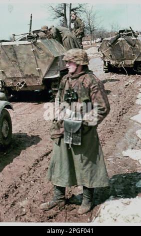 Farbfoto aus dem Zweiten Weltkrieg . Ein Soldat aus der 10. SS Panzer Division Frundsberg steht in der Nähe von zwei SdKfz 251/D Panzerspuren während der gescheiterten Versuche, einen sowjetischen Vormarsch in der Nähe von Tarnopol in der Westukraine vom 1944. April zu besiegen Stockfoto