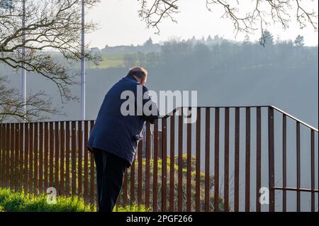 Ein älterer Mann steht allein vor einem Zaun und schaut in die Ferne Stockfoto