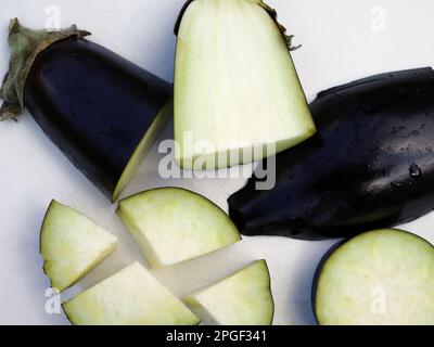 Stücke einer Aubergine auf einem weißen Schneidebrett Stockfoto
